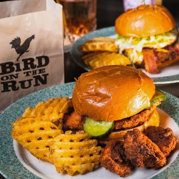 Bird On The Run fried chicken sandwich with waffle fries and nuggets, with another sandwich in the background.