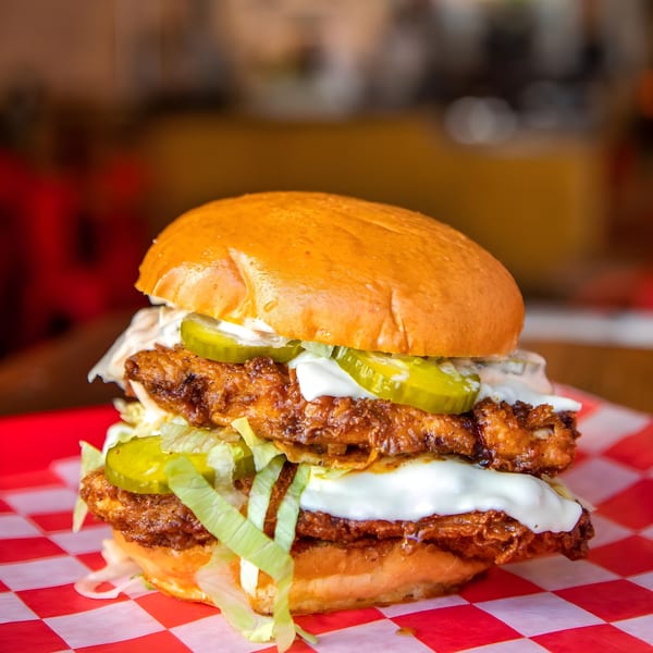 Double-stacked fried chicken sandwich with pickles, lettuce, and white sauce on a red checkered paper.