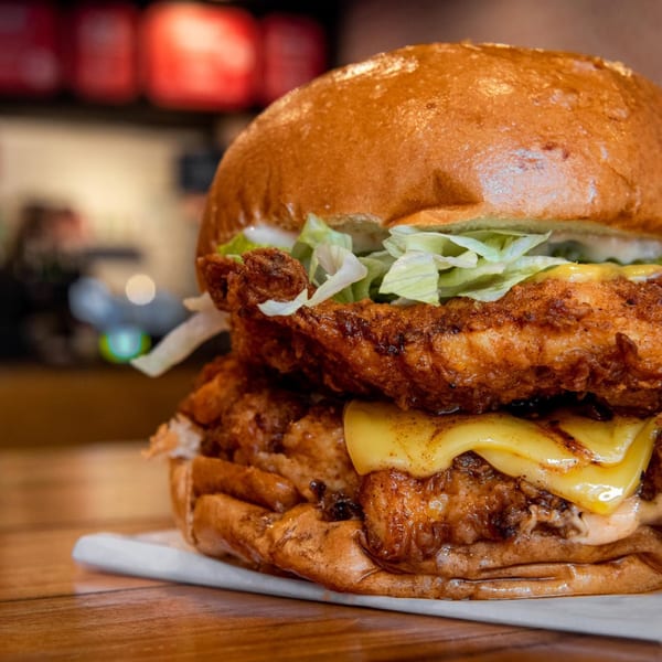 Close-up of a double fried chicken sandwich with melted cheese, lettuce, and sauce on a bun.