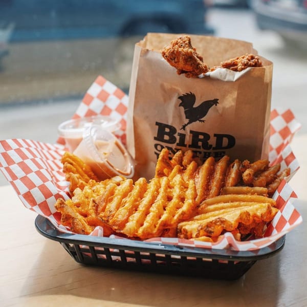 A basket of Bird On The Run fried chicken, waffle fries, and dipping sauces.